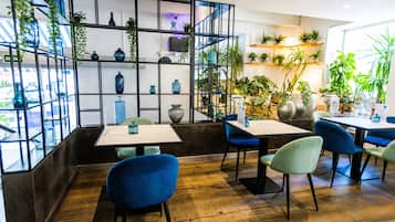 A restaurant interior with wooden flooring, blue and green chairs, and shelves with blue vases and plants.