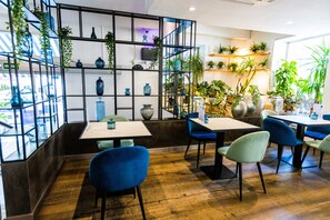 A restaurant interior with wooden flooring, blue and green chairs, and shelves with blue vases and plants. - Hotel 54 Barceloneta (Barcelona)