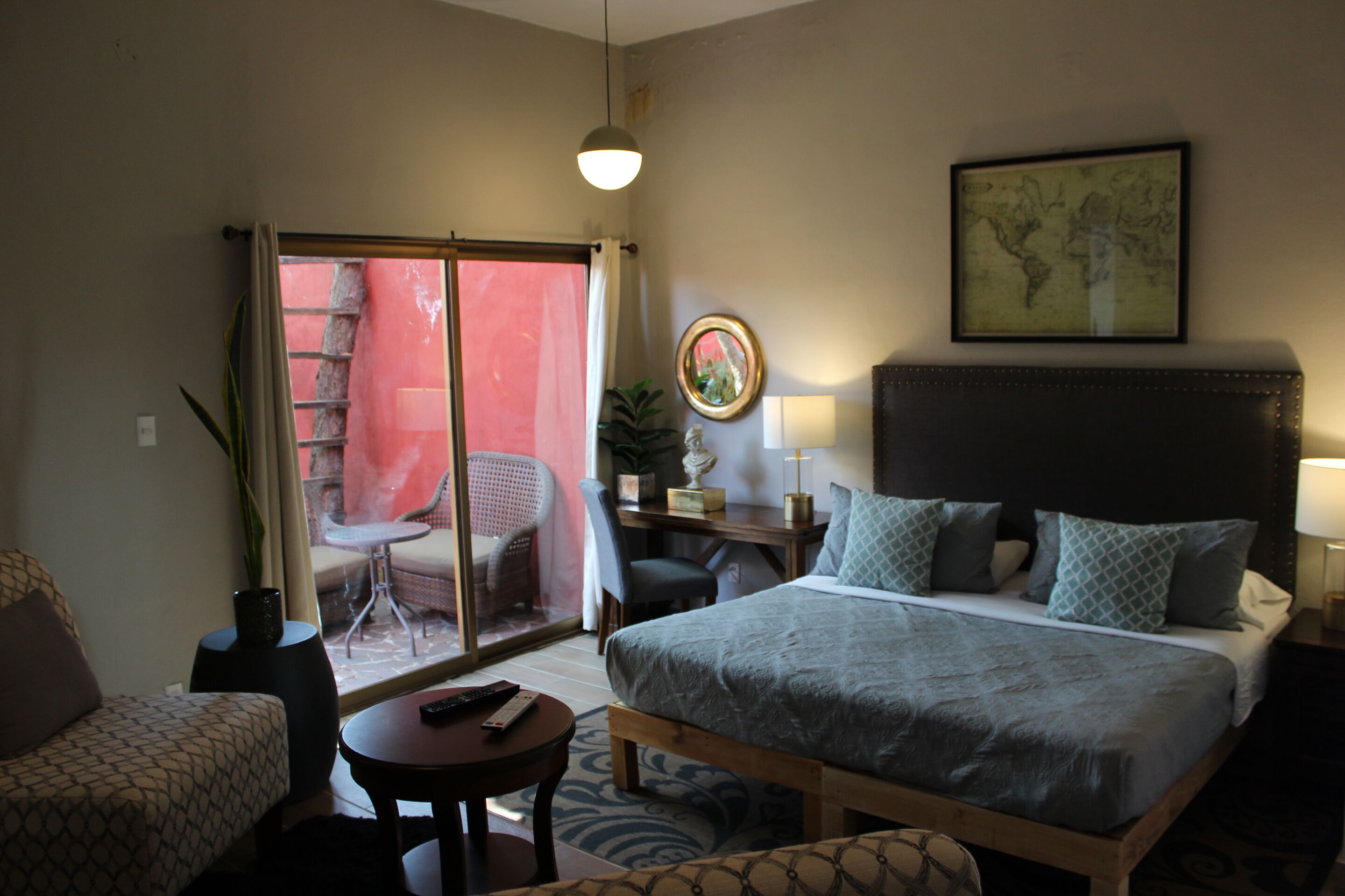 A hotel room with a bed, a desk, a chair, a small table, and a view of the outside.