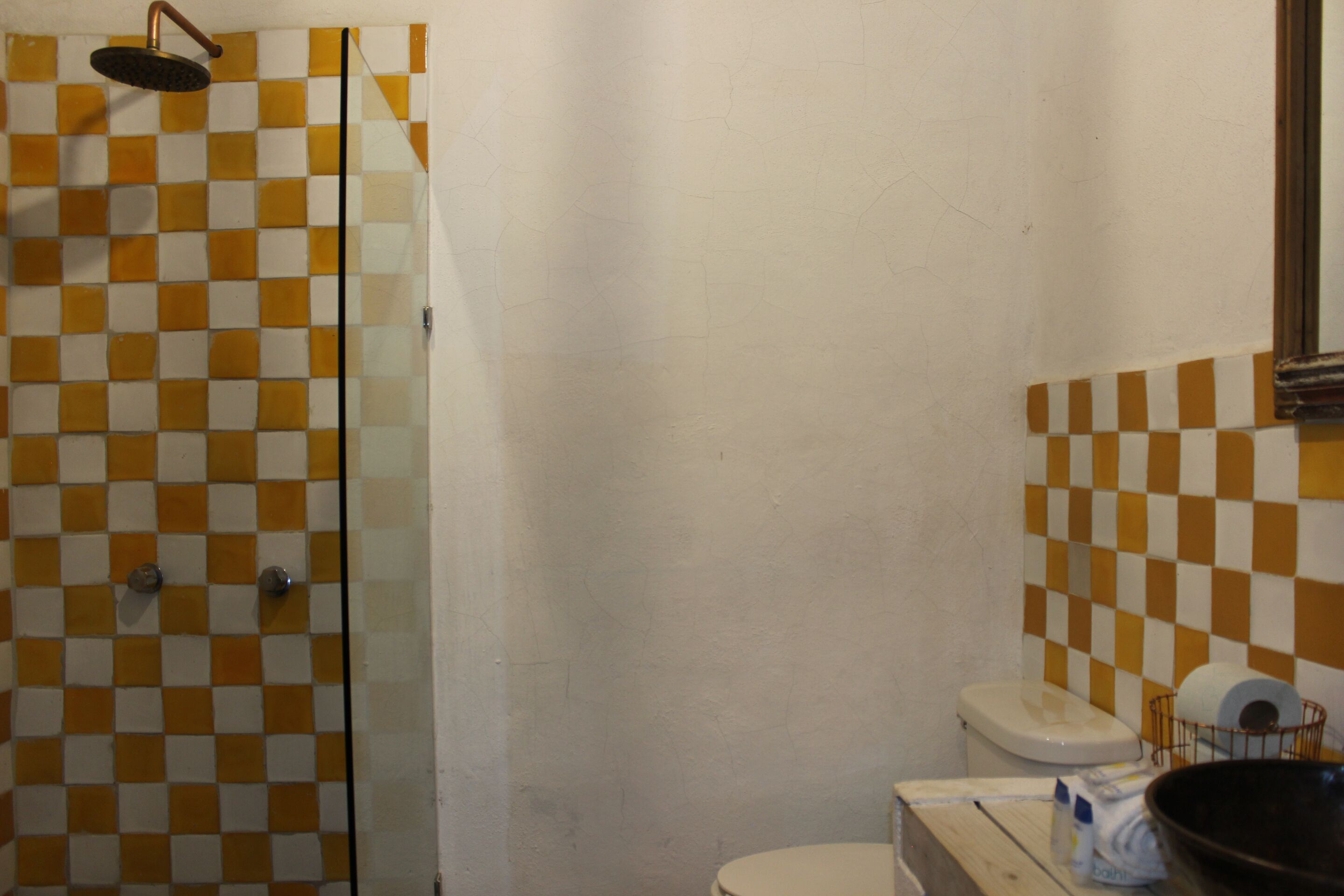 Een badkamer met een betegelde muur in ruitpatroon, een glazen douchecabine, een toilet en een wastafel met een handdoekdispenser.