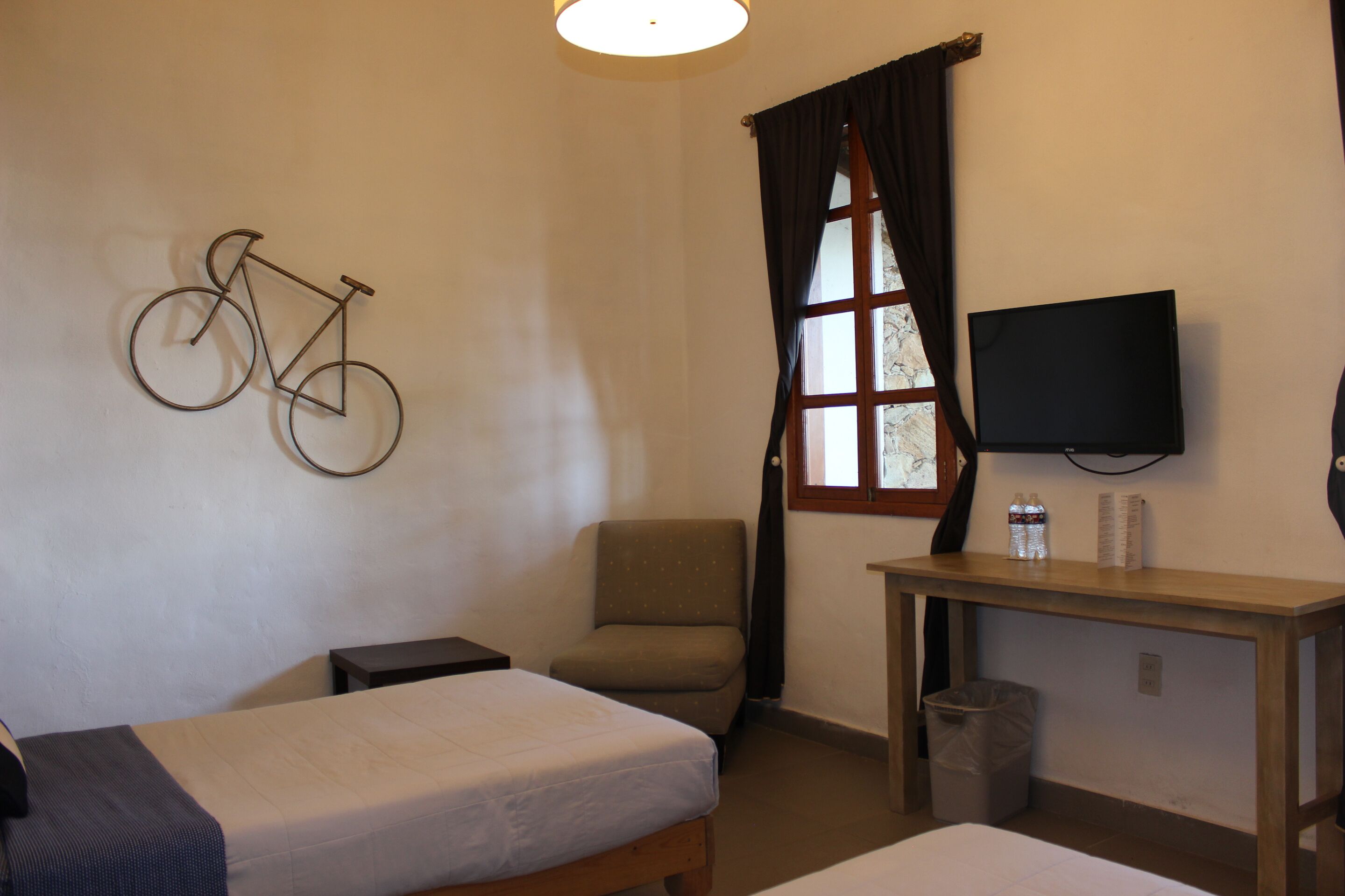 A hotel room with a bed, a chair, a desk, a television, and a bicycle art piece on the wall.