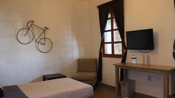 A hotel room with a bed, a chair, a desk, a television, and a bicycle art piece on the wall.