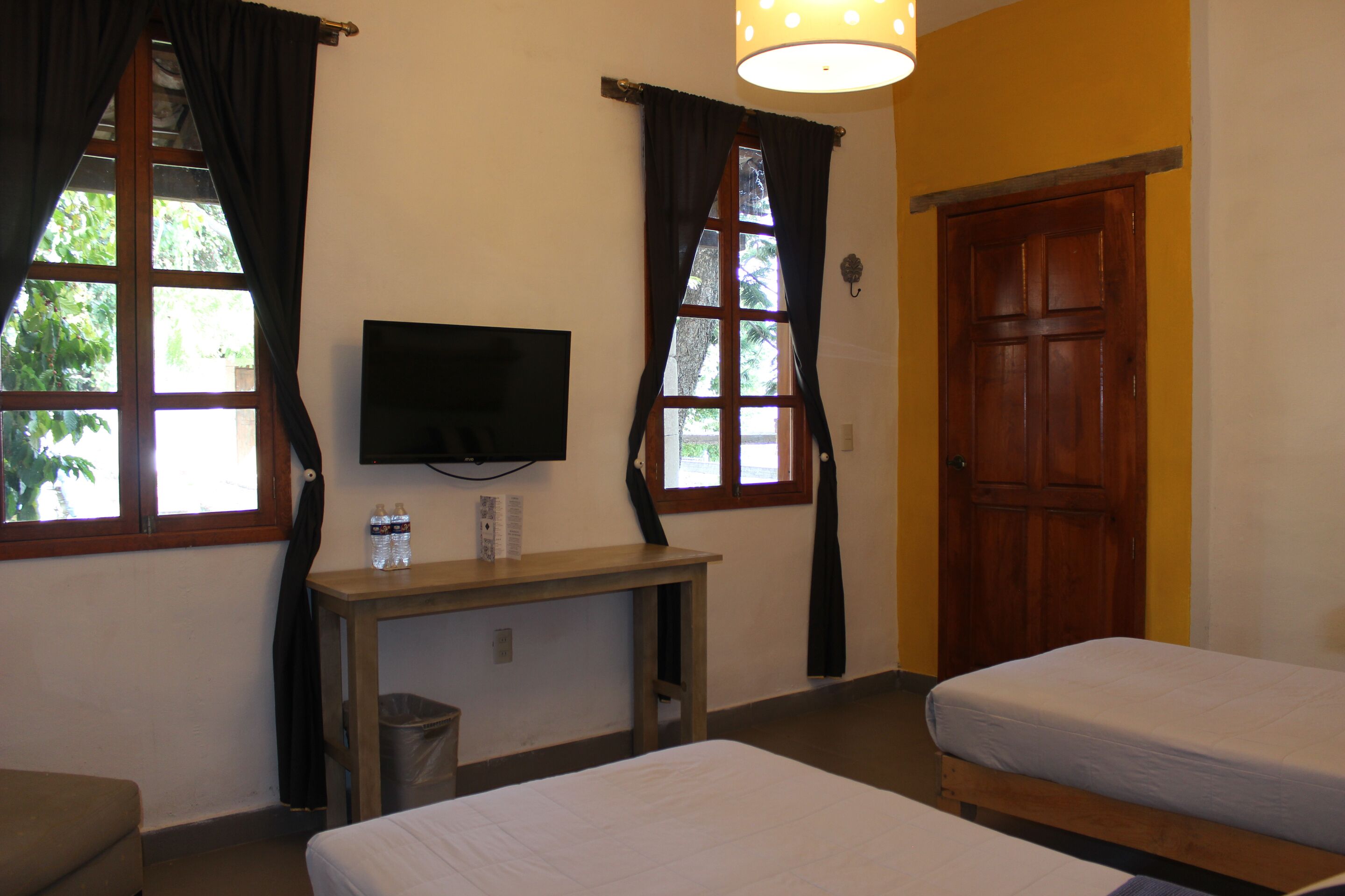 A hotel room with two beds, a TV mounted on the wall, a wooden desk, and a window with curtains.