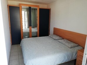 Ein Schlafzimmer mit einem Bett, einem Holz-Kopfteil, einem Nachttisch und einem Kleiderschrank mit Spiegel.