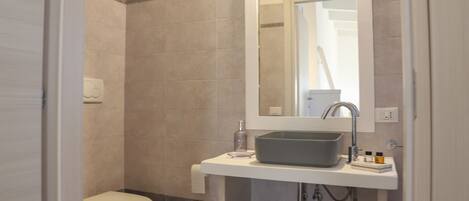 A bathroom with a toilet, a sink with a mirror, and a shower area.