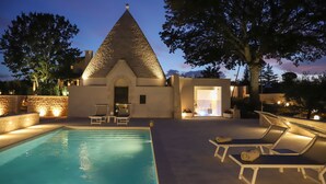 A swimming pool with lounge chairs, a stone wall, and a building with a conical roof. - TD Trullo Roverella Charming Trullo with Pool (Castellana Grotte)