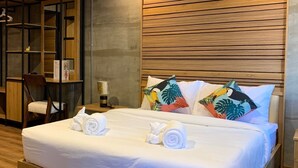 A neatly made bed with white linens and two rolled towels, a wooden headboard, and tropical-themed pillows. - Pinghostel - Adults Only (Chiang Mai)