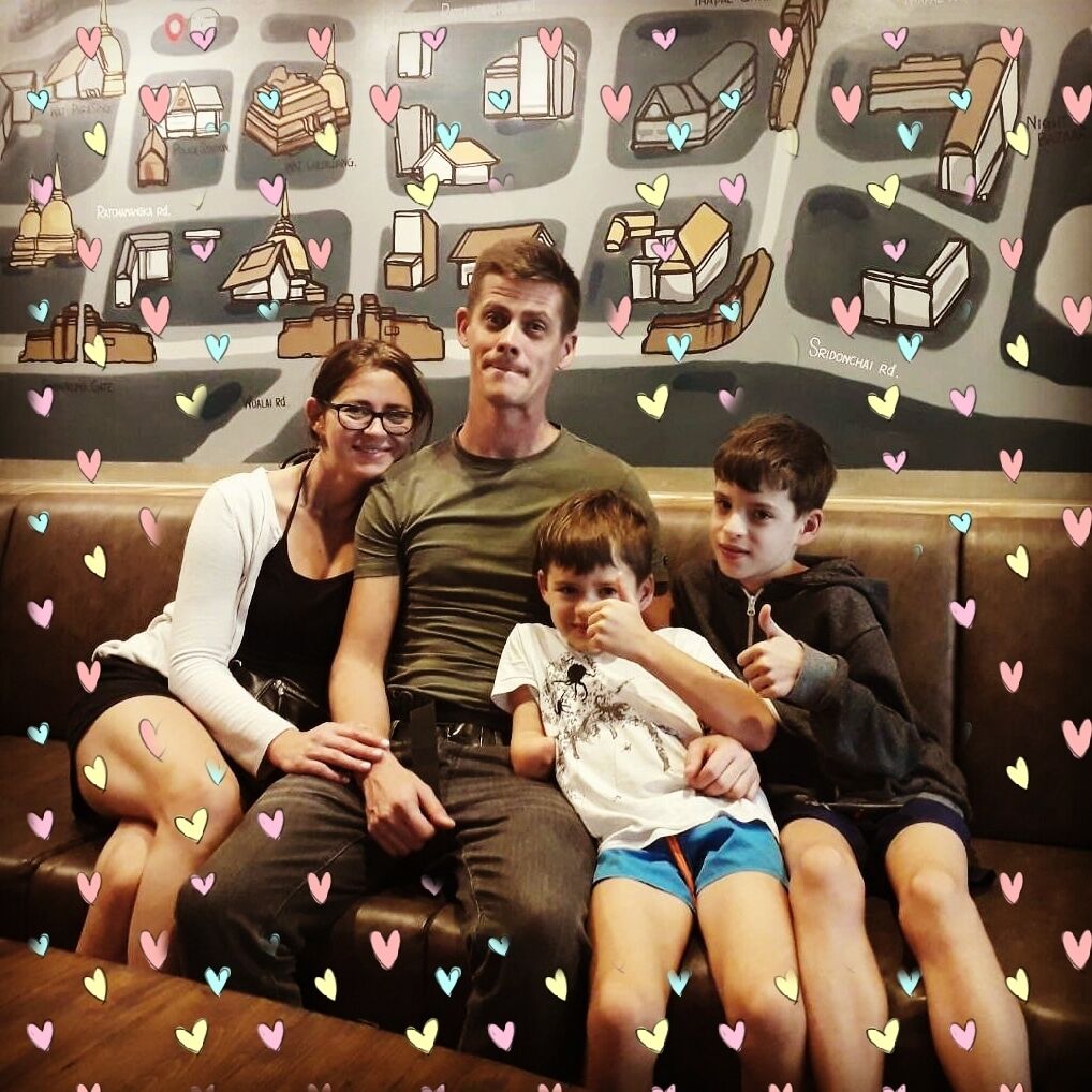 A family sitting on a brown leather couch with a wall decorated with various building illustrations and hearts.