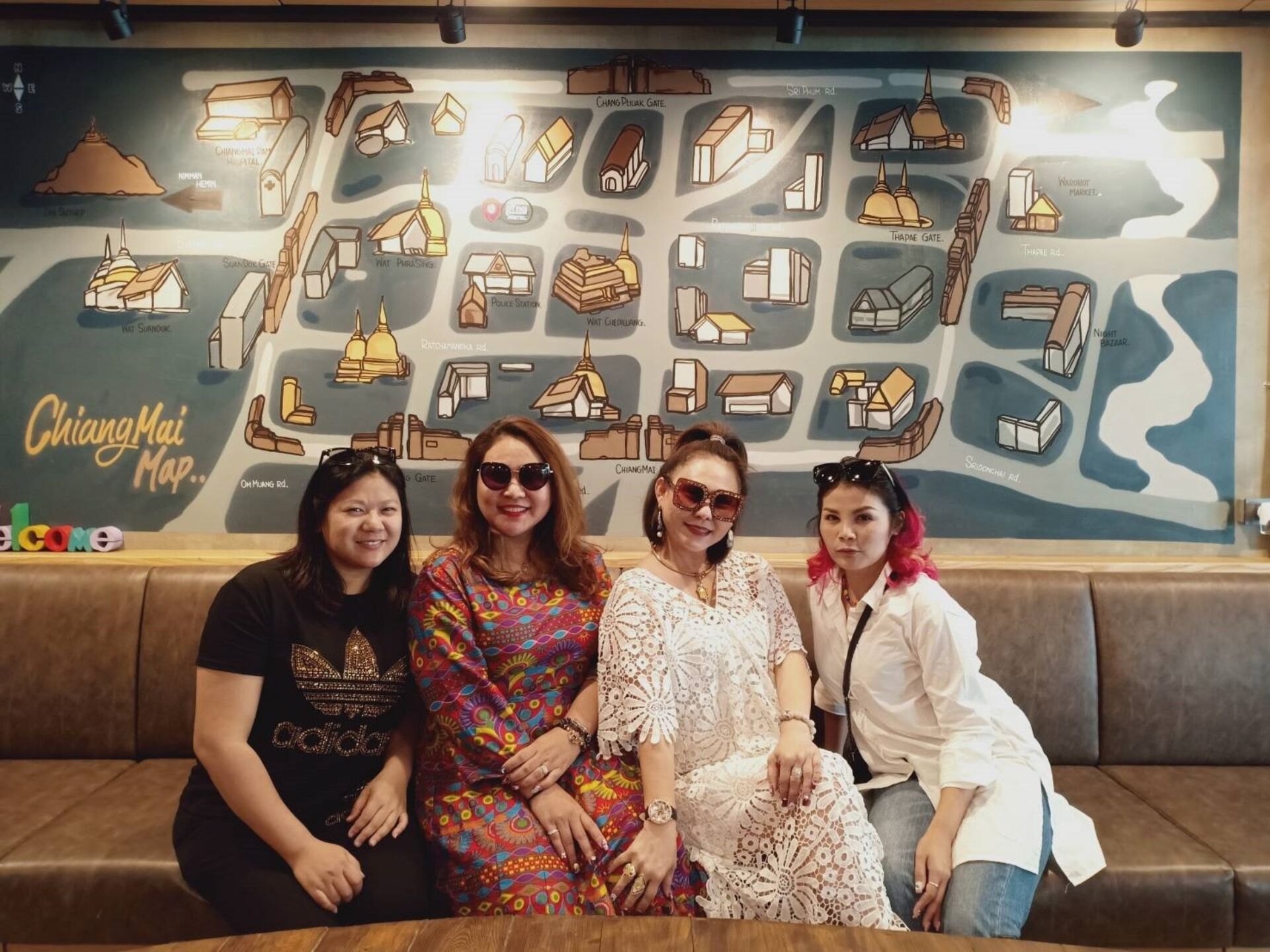 A group of people seated on a couch in front of a wall with a map labeled "Chiang Mai Map."