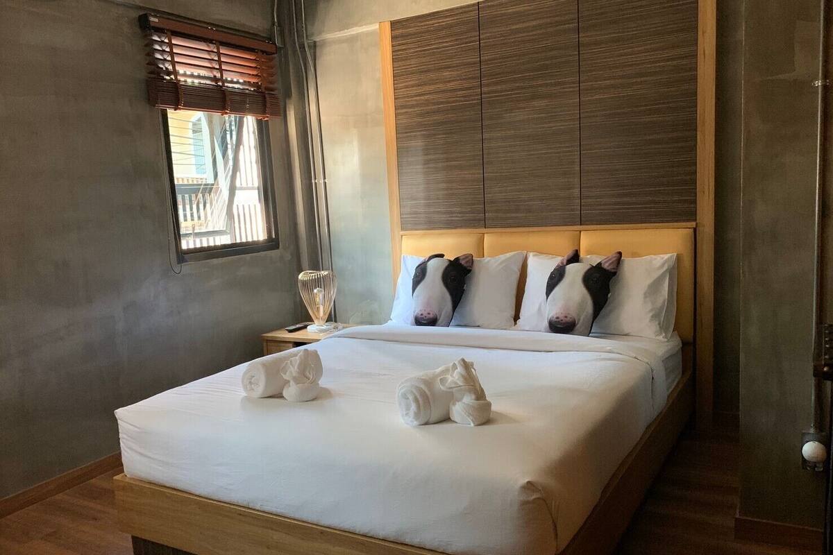 A neatly made bed with towels, a bedside lamp, and a window with blinds.