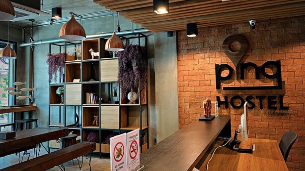 A hostel interior with wooden furniture, shelves with decorations, and a sign reading "pong hostel". - Pinghostel - Adults Only (Chiang Mai)