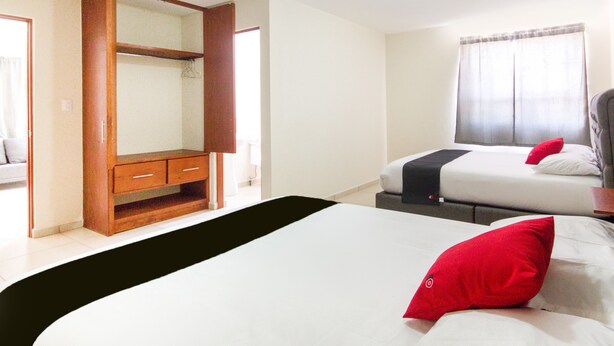 A hotel room with a bed, a wooden wardrobe, and a window with curtains. - Suites del Pozo (San Luis Potosi)
