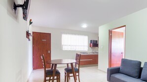 A living room with a sofa and a dining table with chairs. There is a kitchen in the background with a microwave and a window. - Suites del Pozo (San Luis Potosi)