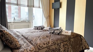 Ett hotellrum med en stor säng, en platt-TV som är monterad på väggen och ett fönster med persienner.