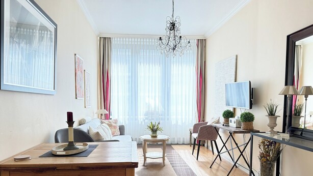 A modern living room with a wooden dining table, a sofa, a TV, and a chandelier. - House by the Sea App. 21 (Westerland)