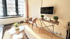 A modern living room with a large window, a flat-screen TV, a wooden coffee table, a comfortable chair, and a small plant. - House by the Sea App. 21 (Westerland)