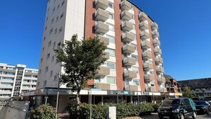 En flervåningsbyggnad med bostäder, balkonger, en tydligt markerad entré och en klarblå himmel.