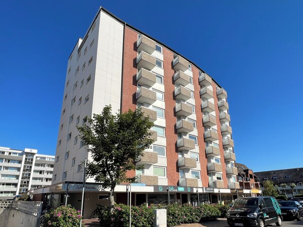 A multi-story residential building with balconies, a visible entrance, and a clear blue sky.