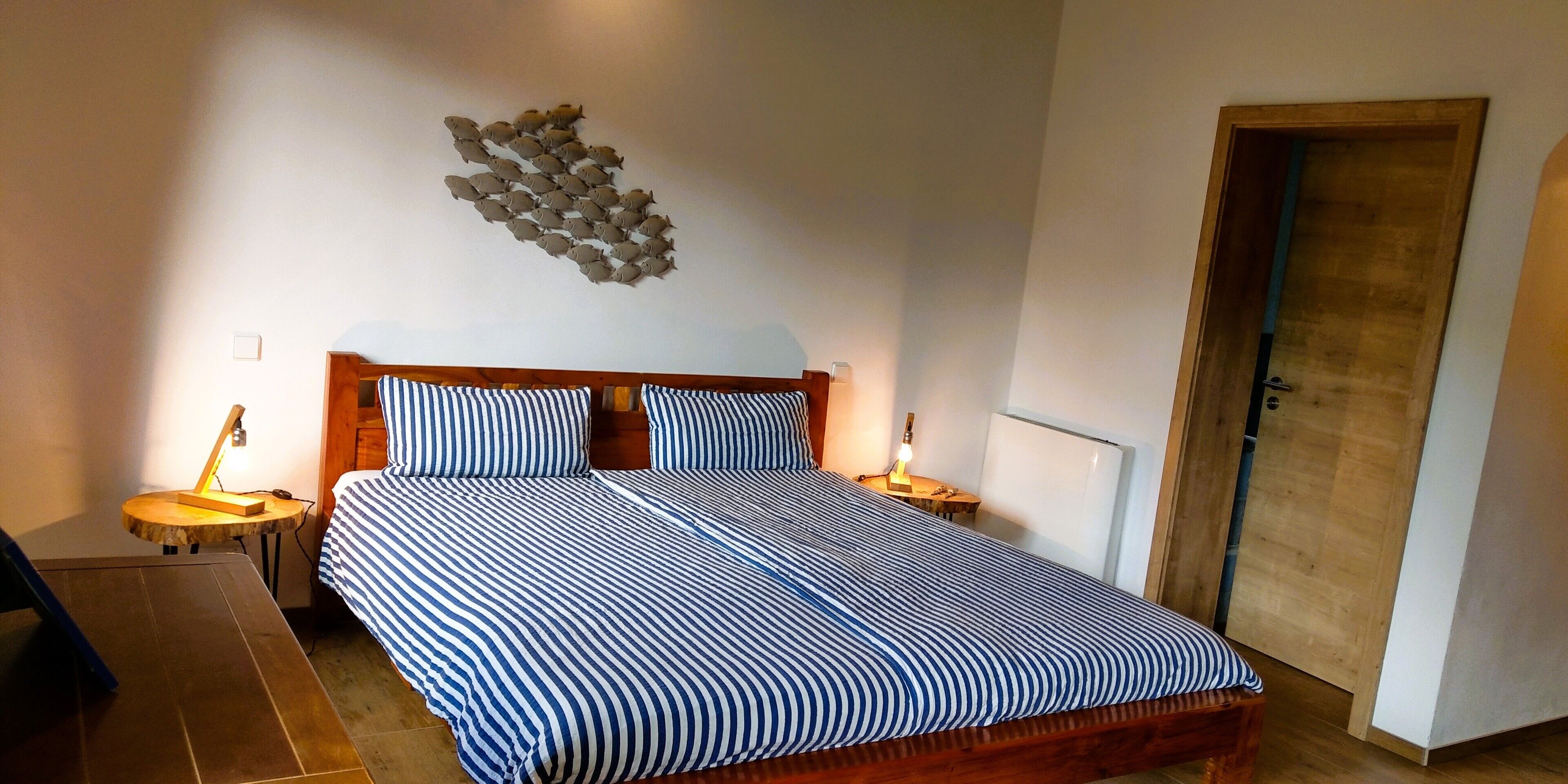 A bedroom with a large bed, two bedside tables, a wooden door, and a wall art piece.