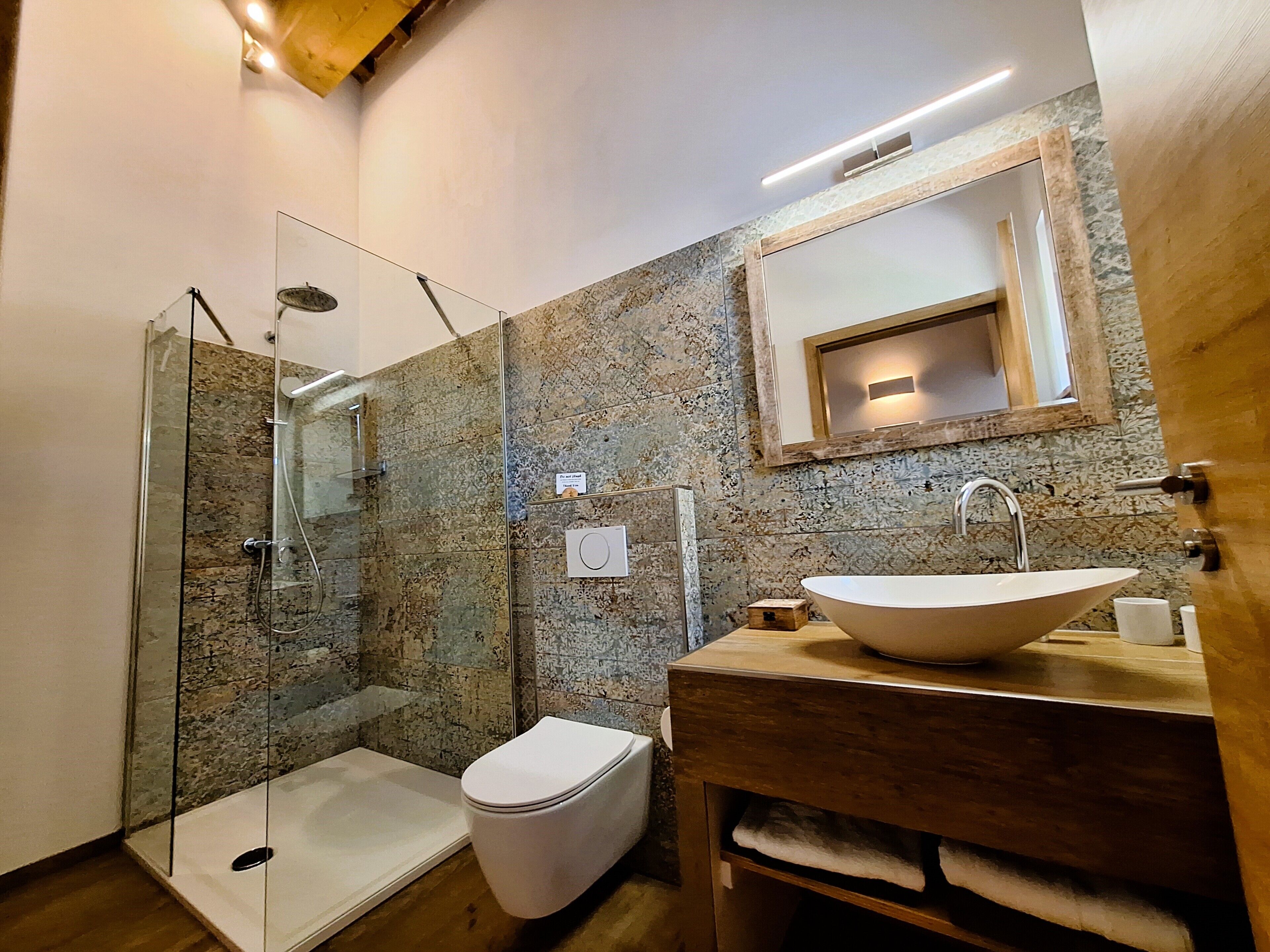 A modern bathroom with a glass-enclosed shower, a wooden vanity, and a large mirror.