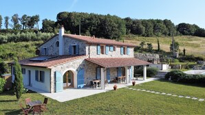 A stone house with a tiled roof, a covered patio with outdoor seating, and a well-maintained lawn. - Fantastic new villa near the sea in one of the most beautiful areas of Tuscany  (Pomaia)