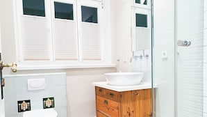 A bathroom with a toilet, sink, wooden cabinet, and a shower area. - Lille Villa App Stars Westerland (Westerland)