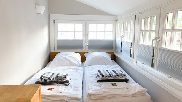 A twin room with two beds, a wooden desk, and large windows with blinds. - Lille Villa App Moon Westerland (Westerland)