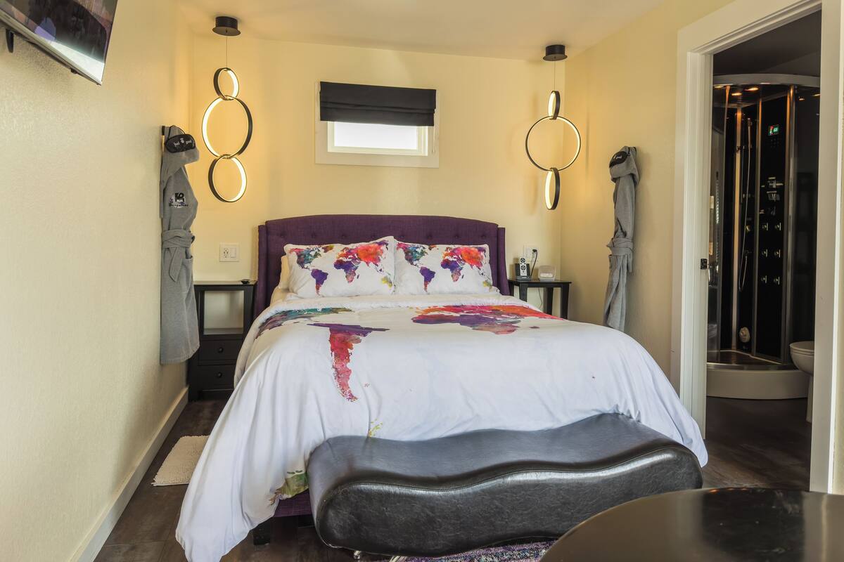 A bedroom with a large bed, a bench, a nightstand, a robe, and a bathroom visible through an open door.