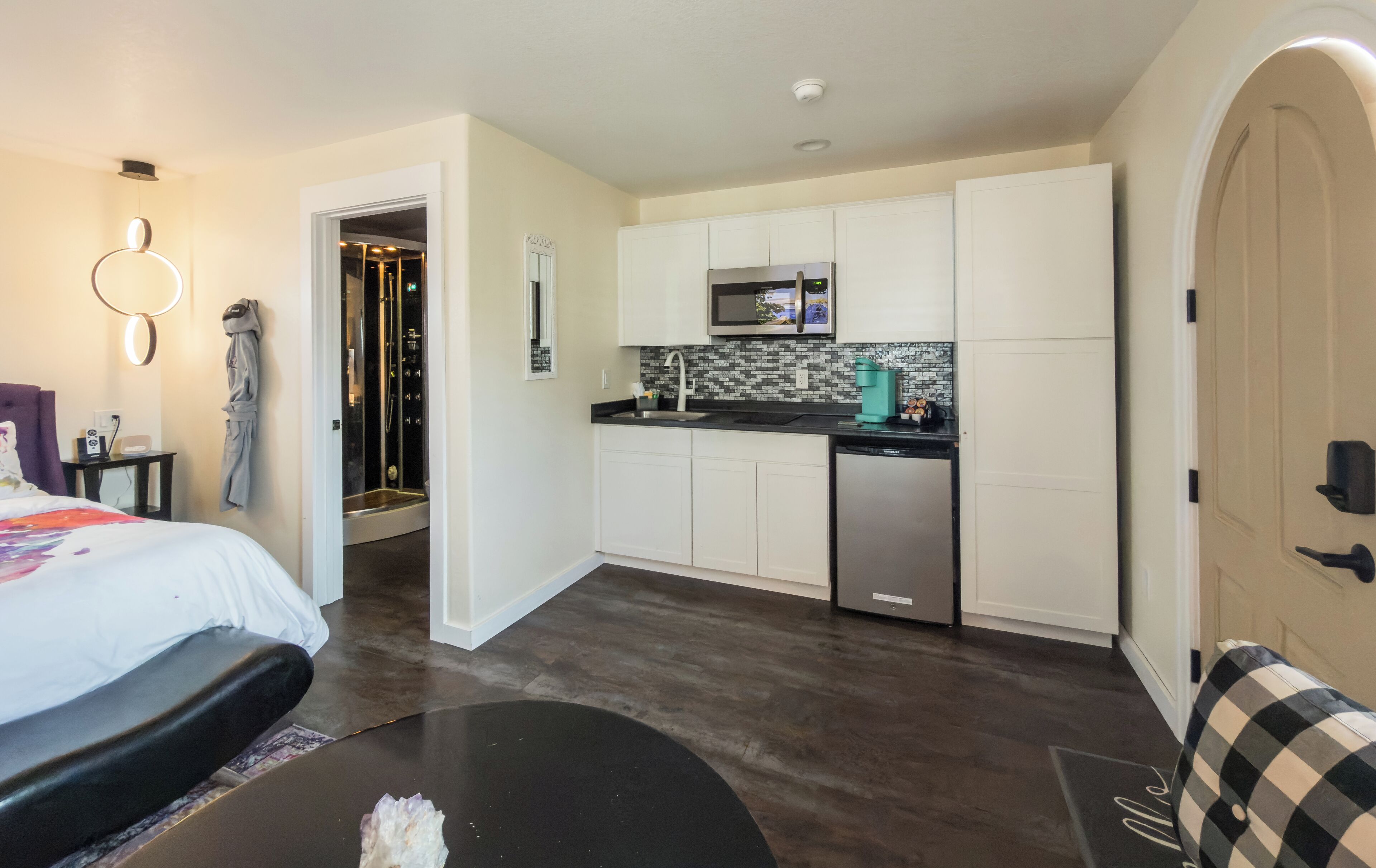 A compact hotel room with a kitchenette, a shower, and a bed.