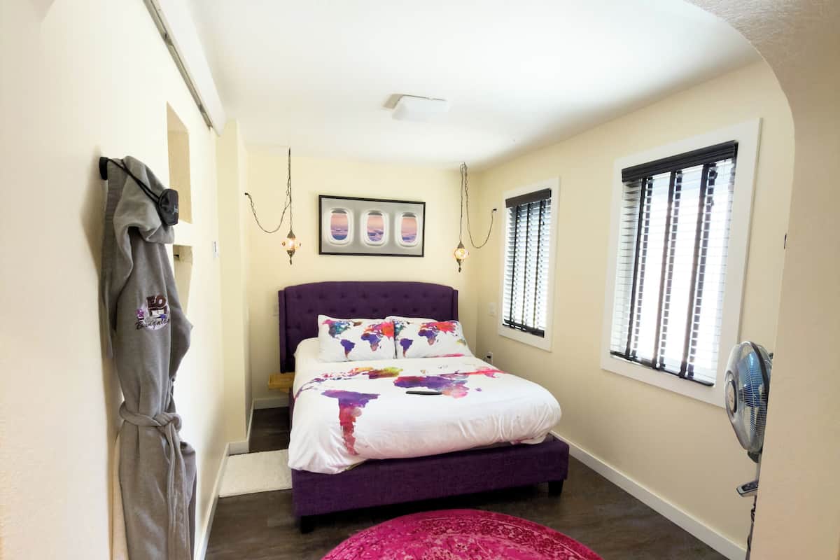 A bedroom with a purple bed, a pink rug, and a gray robe on a rack.