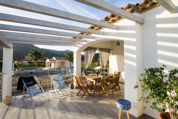 A covered outdoor seating area with a table and chairs, a view of the landscape, and a pergola structure.