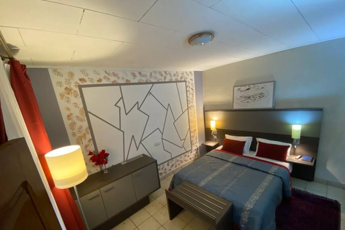 A bedroom with a bed, bedside tables, a nightstand, a lamp, and a wall with a geometric design.