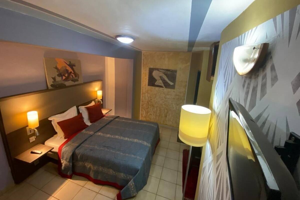 A hotel room with a bed, bedside lamps, a wall-mounted light, and a framed picture.
