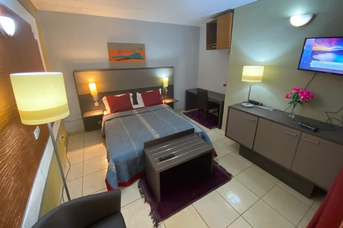A hotel room with a bed, bedside tables, a desk, a TV, and a small seating area.