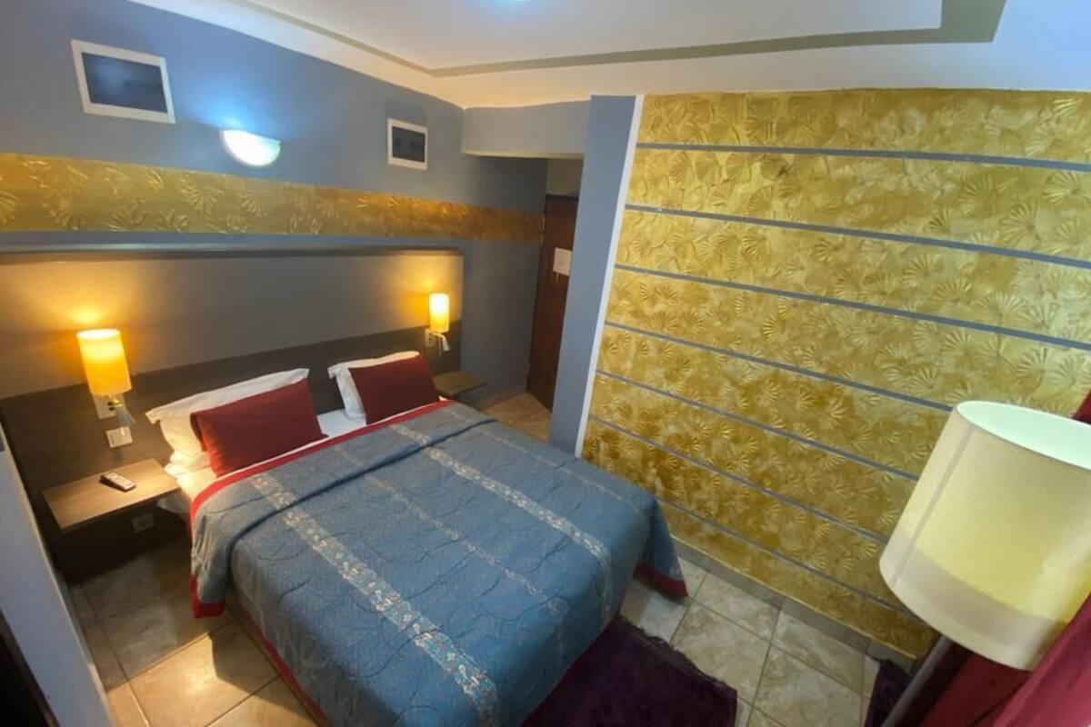 A bedroom with a bed, two bedside lamps, a nightstand, a headboard with a floral pattern, and a wall with a decorative panel.