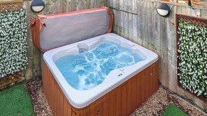 A hot tub with a wooden exterior, surrounded by a wooden fence and green artificial grass.