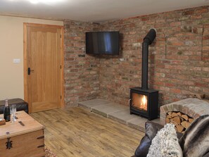 A cozy room with a brick wall, a wooden door, a television mounted on the wall, and a wood-burning stove.