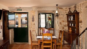 A rustic dining area with a stone wall, a wooden table with chairs, a hanging light fixture, and a staircase. - STONE HOUSE WITH PORCH AND TERRACE  (Laxe)
