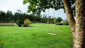 A well-maintained grassy lawn with a swing set in the center, surrounded by trees and a wooden fence. - STONE HOUSE WITH PORCH AND TERRACE  (Laxe)