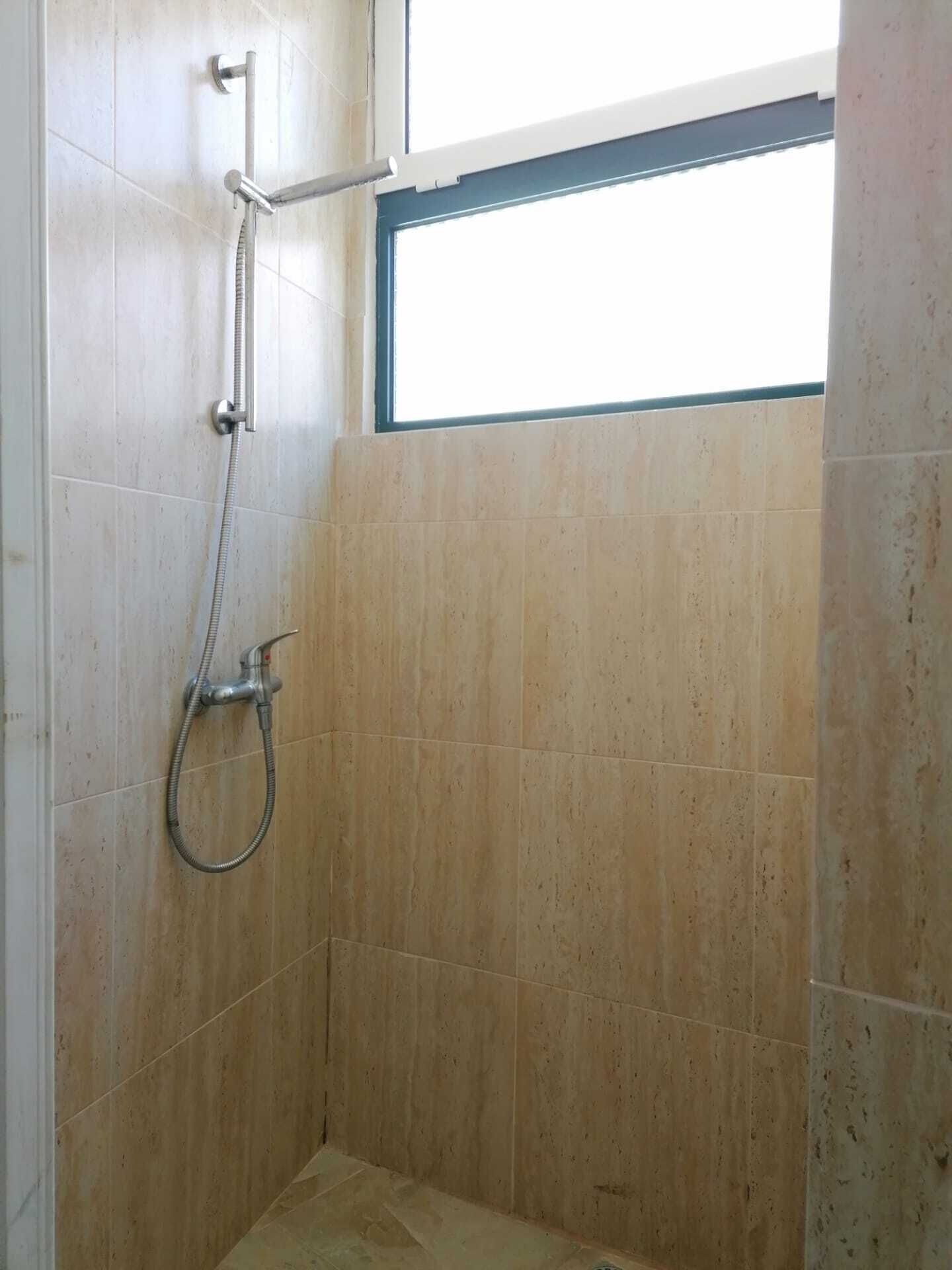 Un petit espace de douche carrelé, avec une fenêtre au-dessus, qui laisse entrer la lumière naturelle.