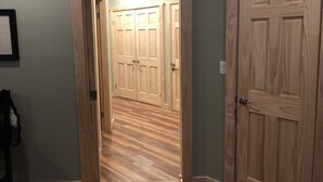 A hallway with wooden flooring, a wooden door on the right, and a door at the end leading to a room with a light fixture. - Naples Valley Getaway-Private home with hot tub.   (Naples)