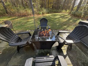 An outdoor patio with a glass-top table, two chairs, and a fire pit.