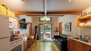 A kitchen with wooden cabinets, a black leather sofa, and a dining area with a table and chairs. - Hot Tub in the treetops with Timber Framed 2 bedroom cabin hidding in the woods (Victor)