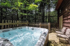 A hot tub surrounded by a wooden deck, with a wooden fence and chairs.