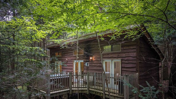 A wooden cabin with a deck and a small porch, surrounded by trees. - Hot Tub in the treetops with Timber Framed 2 bedroom cabin hidding in the woods (Victor)