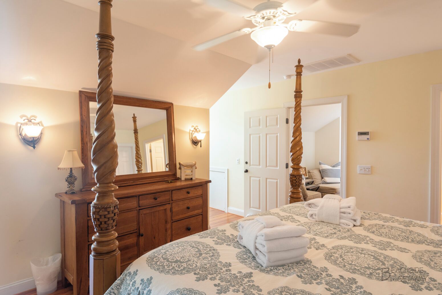A bedroom with a four-poster bed, a wooden dresser, and a ceiling fan.