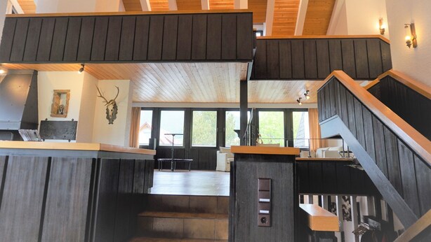 Ein geräumiger Innenraum mit hoher Decke, Holzbalken und einer zentralen Treppe.