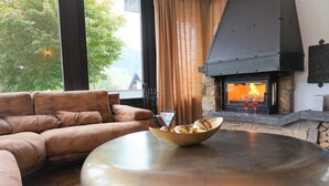 Ein gemütliches Wohnzimmer mit Kamin aus Stein, einem Ledersofa und einem runden Tisch mit einer Schüssel Brot.