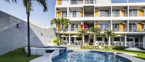 Un hotel con piscina, mobiliario exterior y un edificio de varios pisos con balcones.