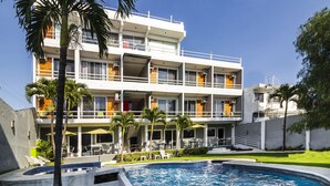 A multi-story hotel with a swimming pool, outdoor seating, and palm trees.